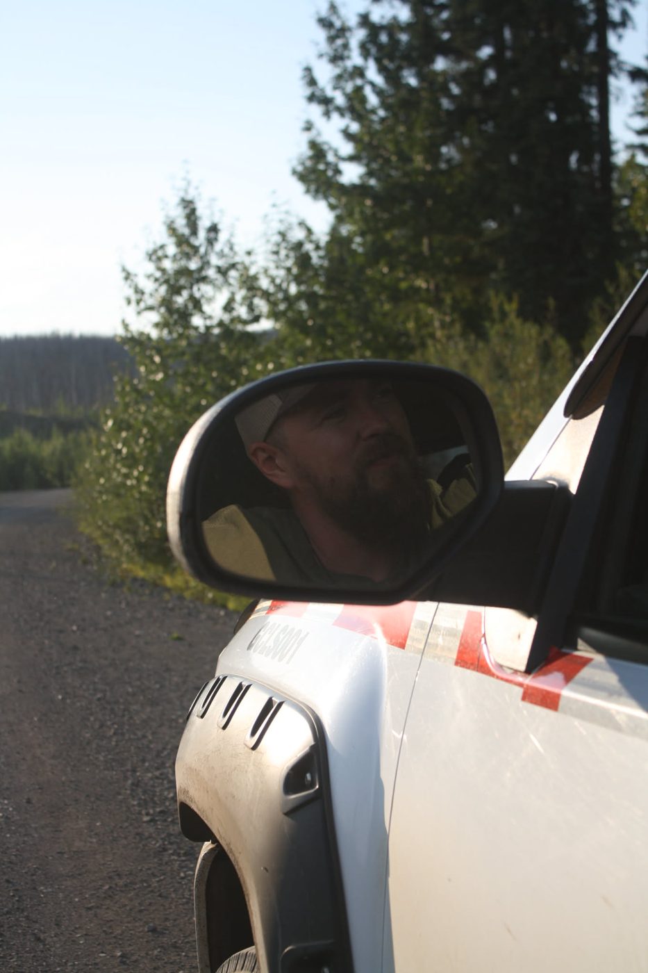 Daniel reflected in the truck mirror on a gravel road